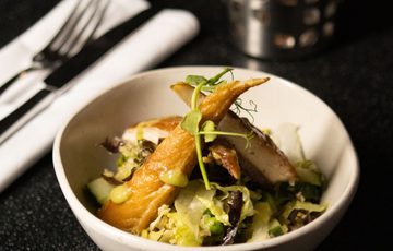 A bowl of smoked mackerel salad on a dark table