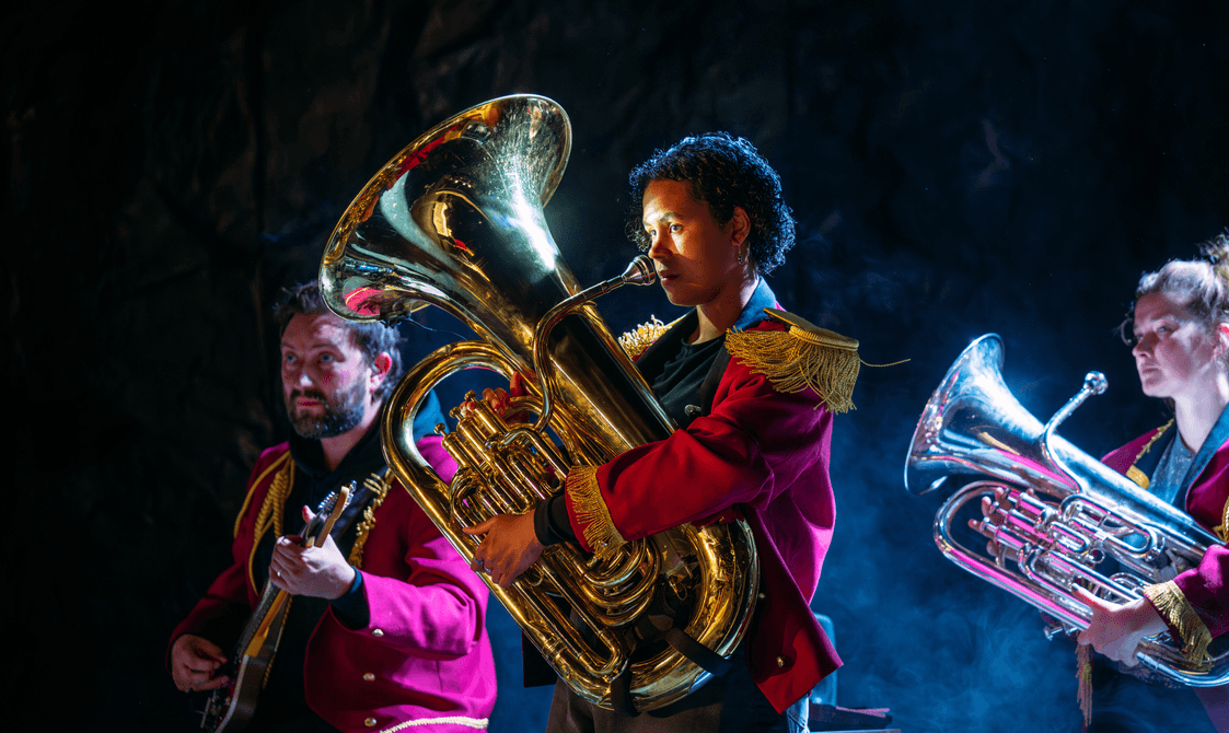 KELI production photo of three people in red coats holding brass instruments