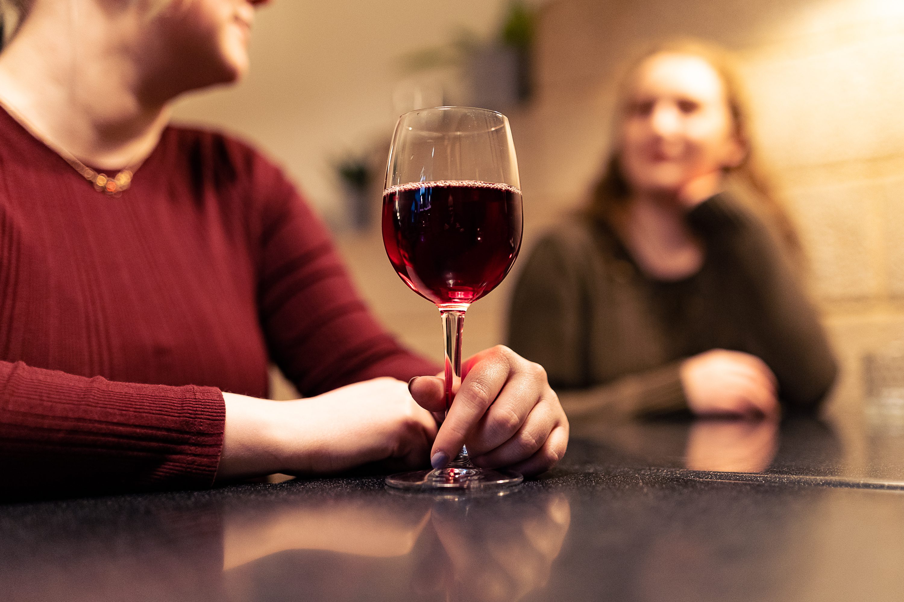 A woman wearing a red top sitting at a black table with a glass of wine