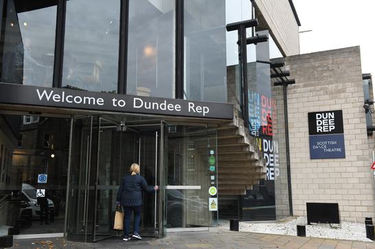 A welcome to Dundee Rep sign above a revolving door as a woman enters with large glass windows above