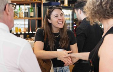 A woman in a black shirt and jeans, smiles and shakes hands with another person in a social setting.