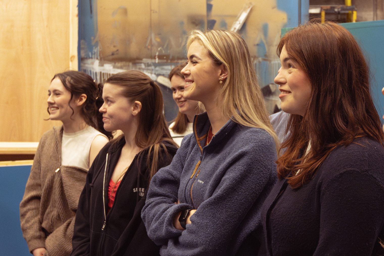 A group of students smile facing to the left of the image in a brightly lit room