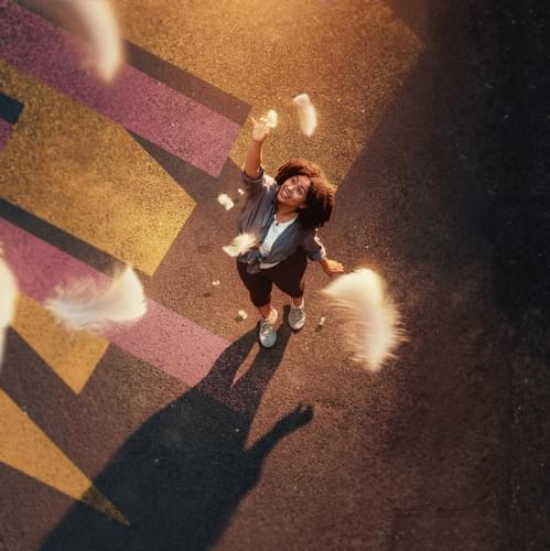 A woman from birds-eye view looks up trying to catch feathers falling from the sky