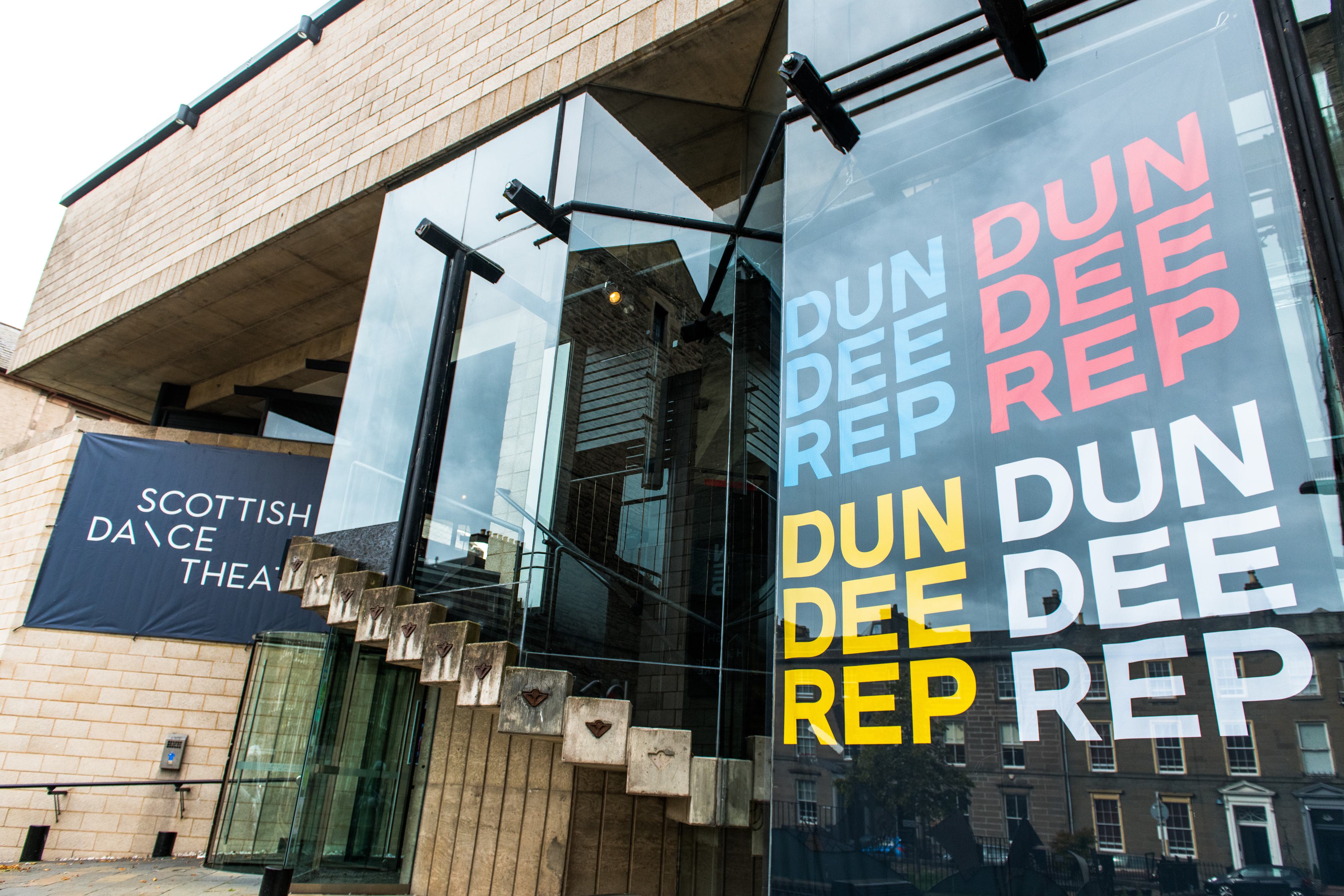 This photo shows the front exterior of Dundee Rep and Scottish Dance Theatre, featuring a large banner in the window reading "Dundee Rep" in different colours and a wall banner which reads "Scottish Dance Theatre"