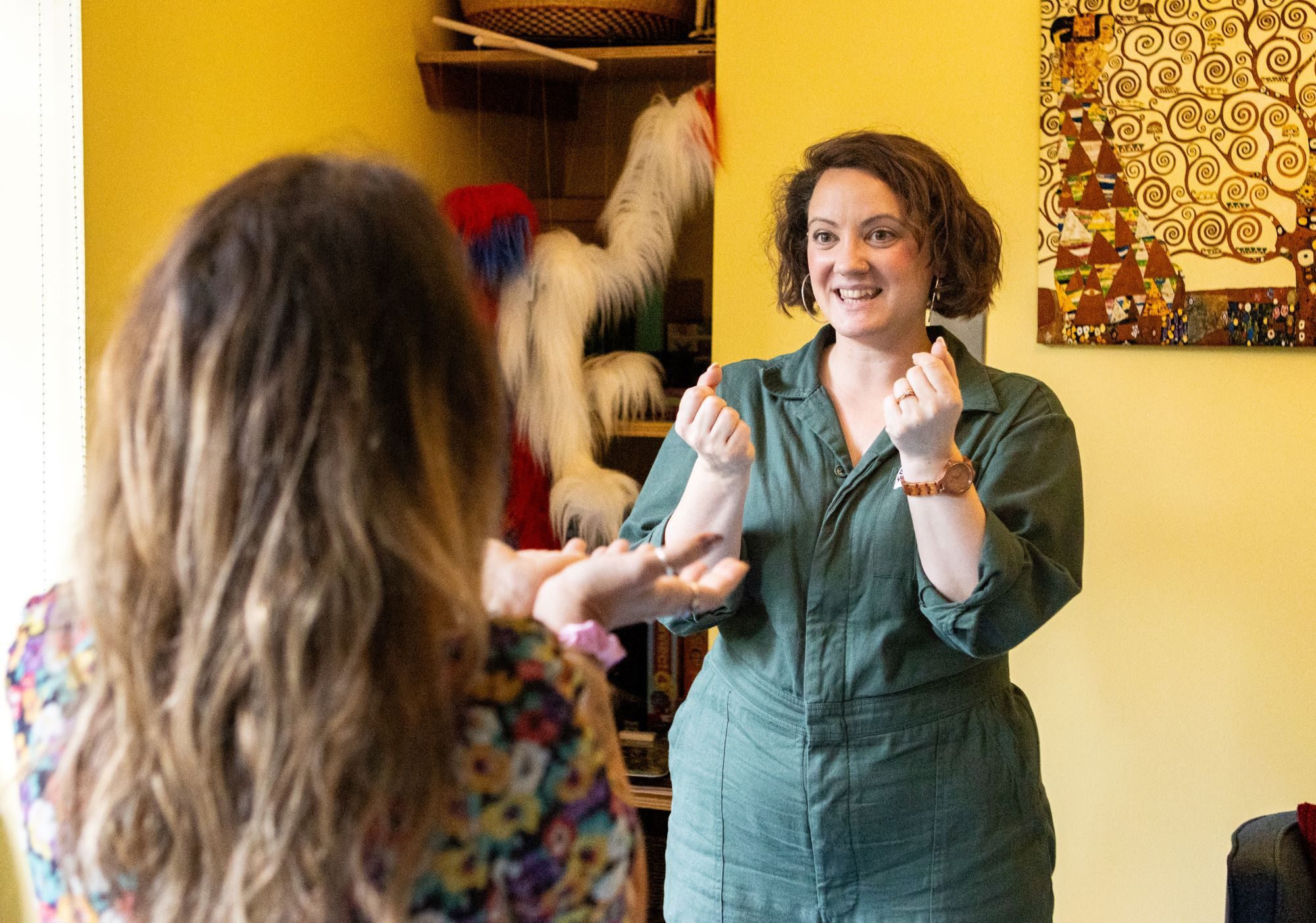 Two women engaging in expressive therapy session, with hand gestures and warm smiles in a creative space.