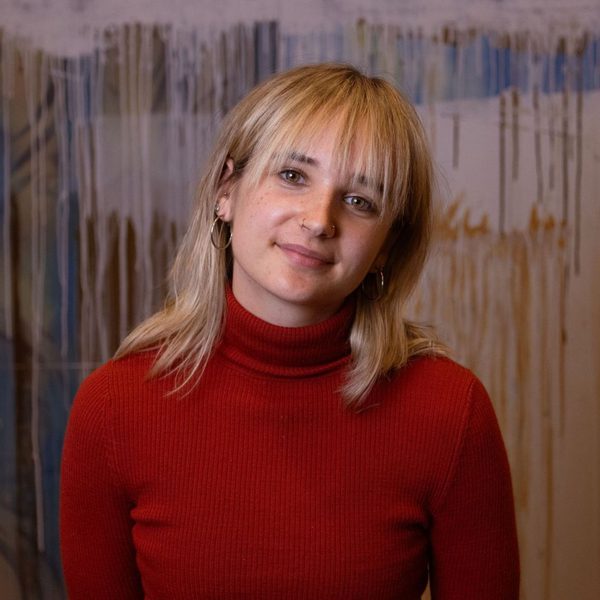 Picture of Caitlin Macleod, Apprentice Dancer with Scottish Dance Theatre, smiling at camera in front of a painted wall