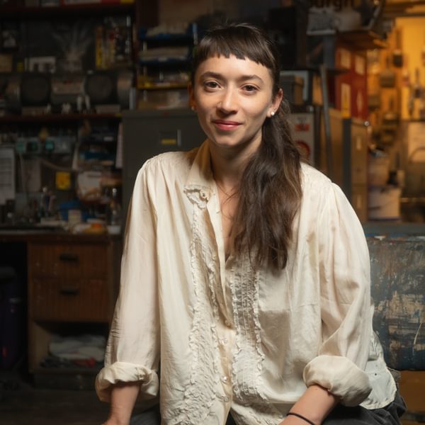 Faith Prendergast, a person with long brown hair wearing a white shirt smiles at camera