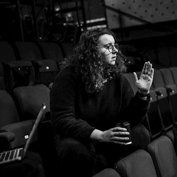 Black-and-white photo of director Joanna Bowman in action, seated in an empty theatre auditorium.