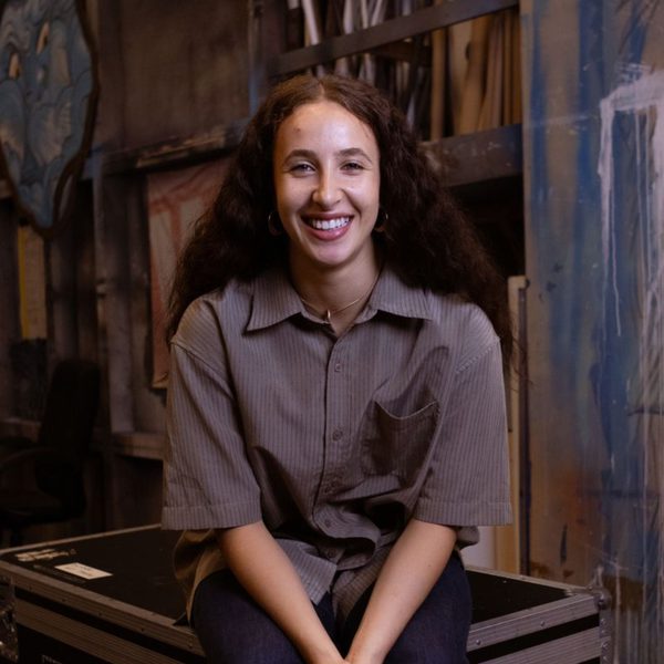 Picture of Jemima Colin, Apprentice Dancer with Scottish Dance Theatre, smiling at camera sitting on a flight case