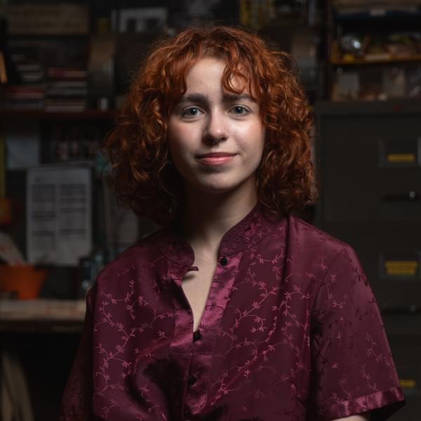 Lara Peres Rocha, a woman with curly ginger hair wearing a burgundy shirt smiles at camera