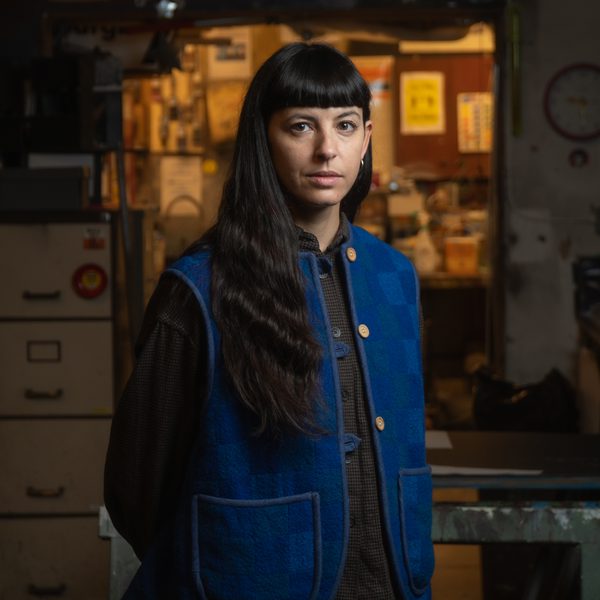 Stefania Pinato, a woman with long black hair wearing a blue vest looks seriously at camera
