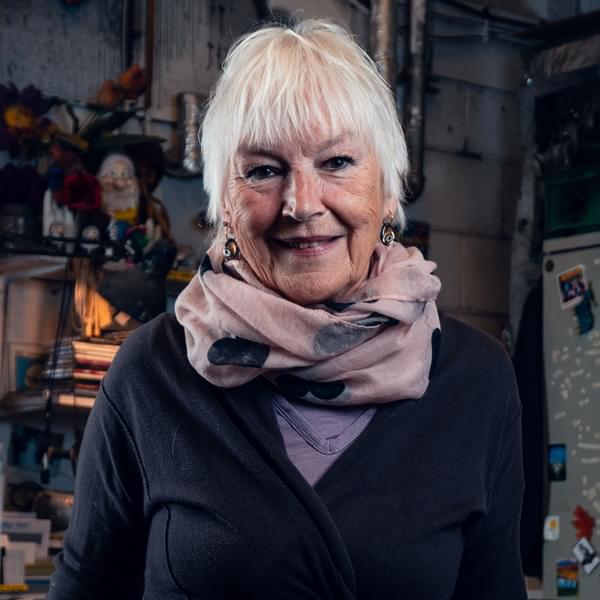 Headshot of Ann Louise Ross, a woman with short white hair, wearing a blue cardigan and pink scarf