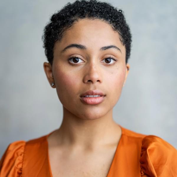 Headshot of Danielle Jam, a woman with short dark hair wearing an orange top on a light grey background