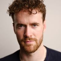 Headshot of Murray Fraser, a man wearing a black tshirt with ginger curly hair, beard and moustache