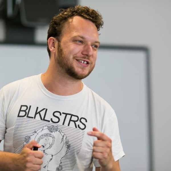 Image of Olvier Emanuel, a man with short dark hair and beard wearing a white tshirt