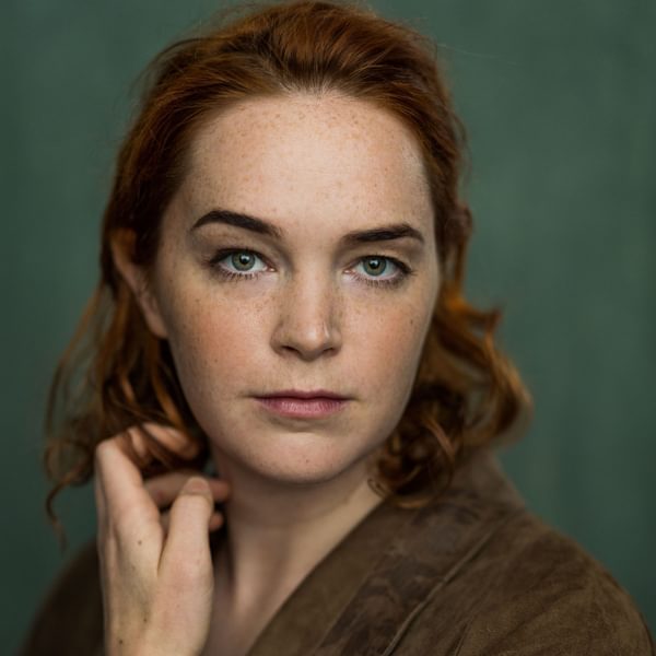 Headshot of Rori Hawthorn, a woman with short ginger hair wearing a dark green top on a green background